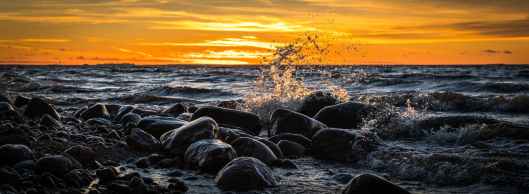 waves splashing at stones on beach during sunset