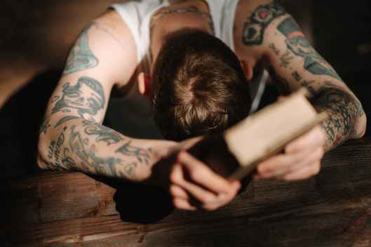 a tattooed man praying while holding a book