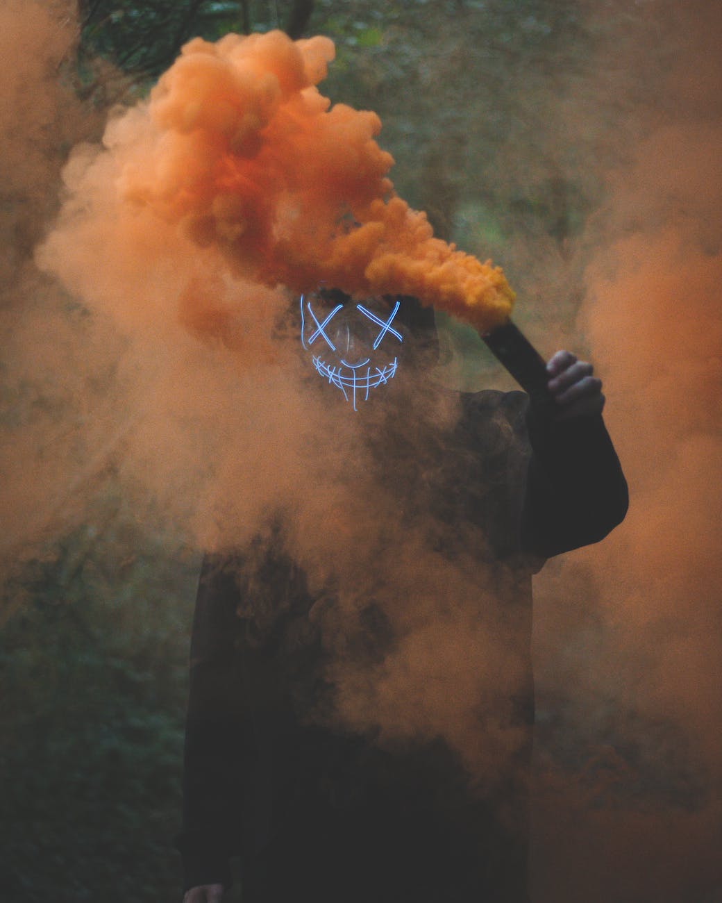 person wearing mask holding colored smoke bomb