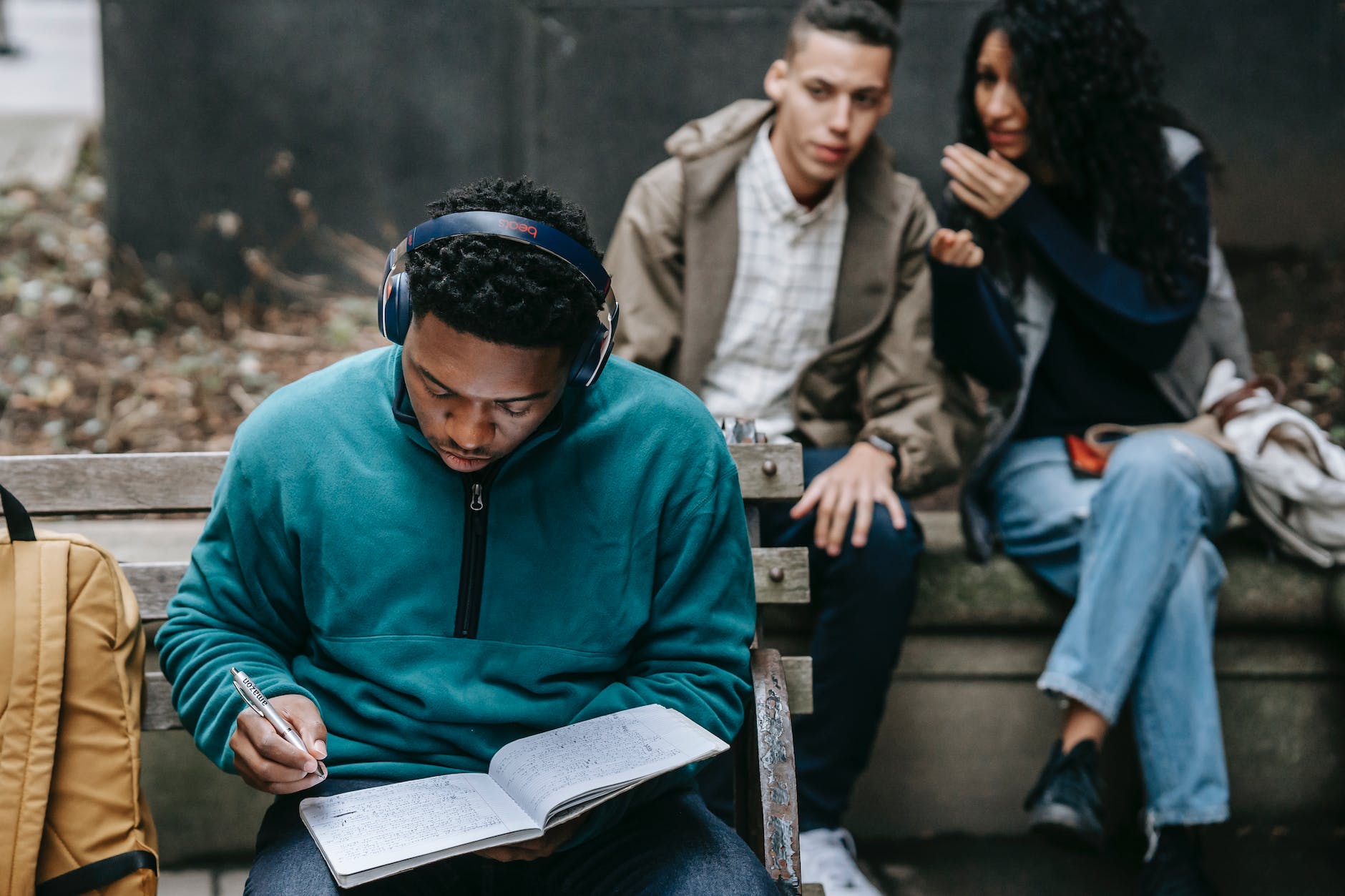 focused black guy preparing for exams in park near curious groupmates