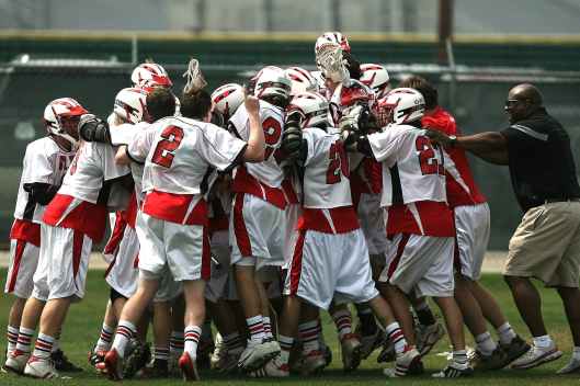 group of lacrosse players celebrating with coach during daytime