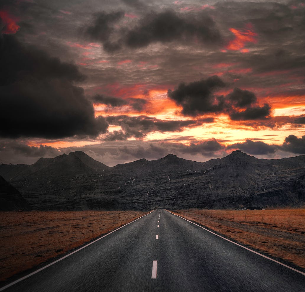 black asphalt road near mountains under cloudy sky